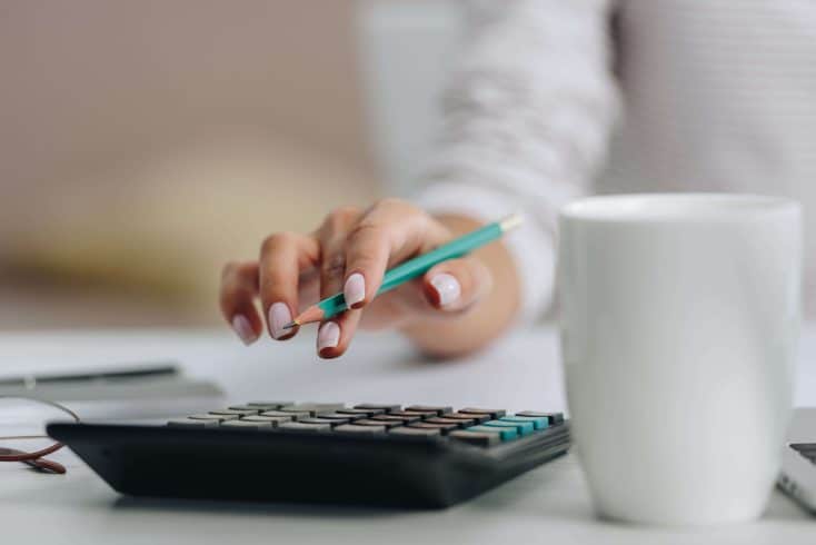 Mão feminina com lápis na mão, usando calculadora