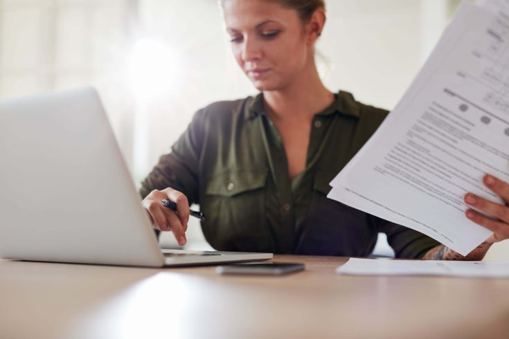 Jovem com documentos trabalhando no laptop