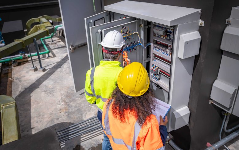 Engenheiros inspecionando os painéis de distribuição de energia de uma fábrica.